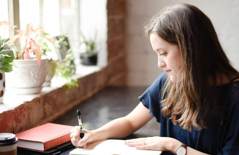 A woman journaling by a bright window